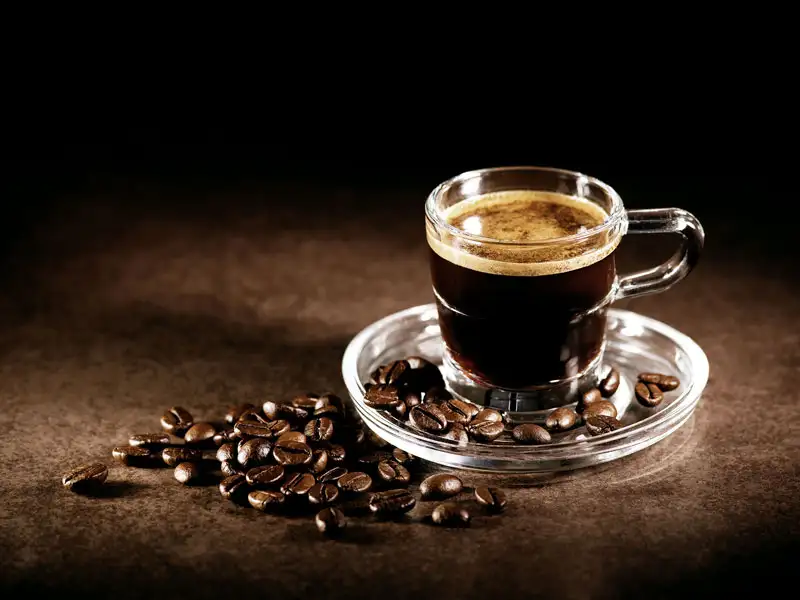 Tasse d’espresso dans un verre avec crema, entourée de grains de café